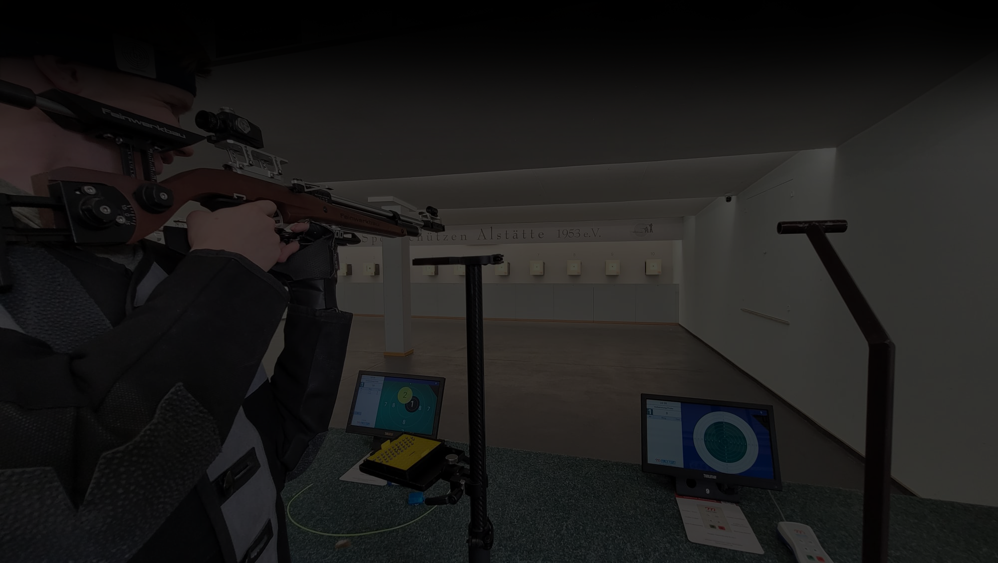 Mann zielt mit Gewähr auf eine Zielscheibe. Auf dem Bild liegt eine schwarze transparente Fläche