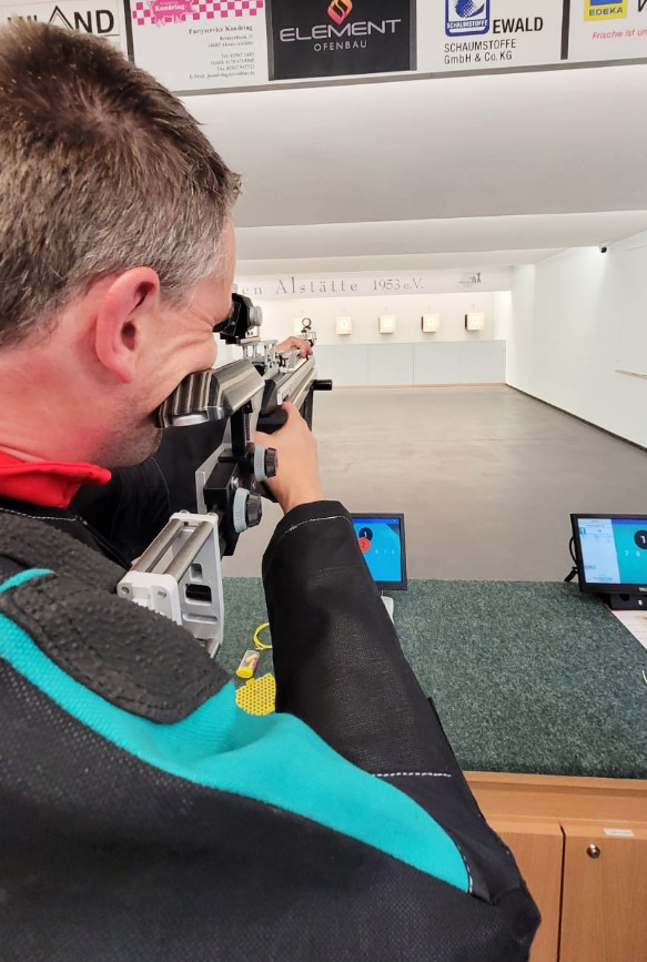 Mann mit Rücken zur Kamera schießt auf Zielscheibe mit Gewehr_